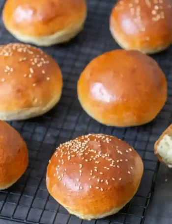 Frisch gebackene Brioche Brötchen und Burger Buns mit glänzender Kruste und Sesam auf einem Gitter zum Abkühlen.