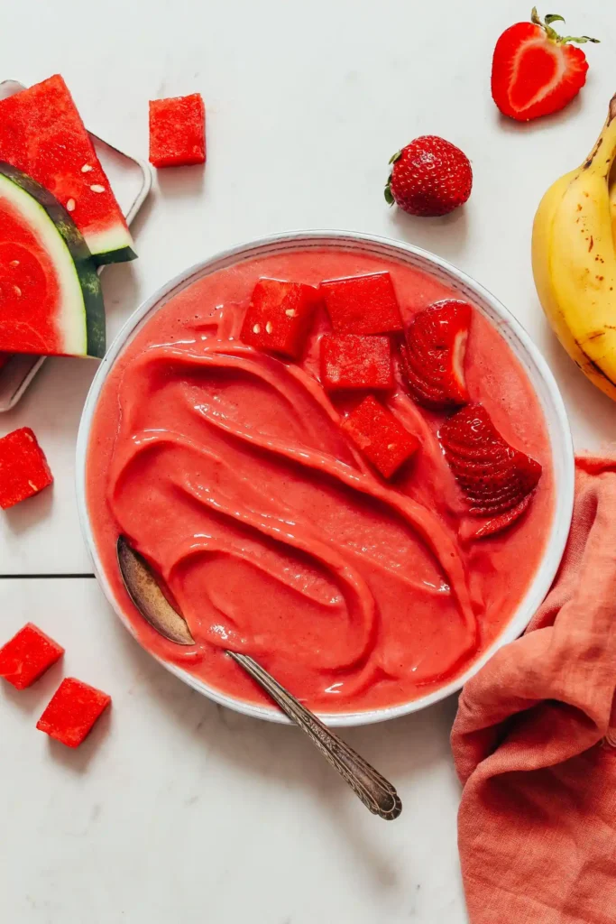 Wassermelonen-Erdbeer-Sorbet in einer weißen Schale mit Löffel, umgeben von frischen Erdbeeren, Bananenstücken und Wassermelonenwürfeln – cremiger süßer Snack in 5 Minuten ohne Backen.