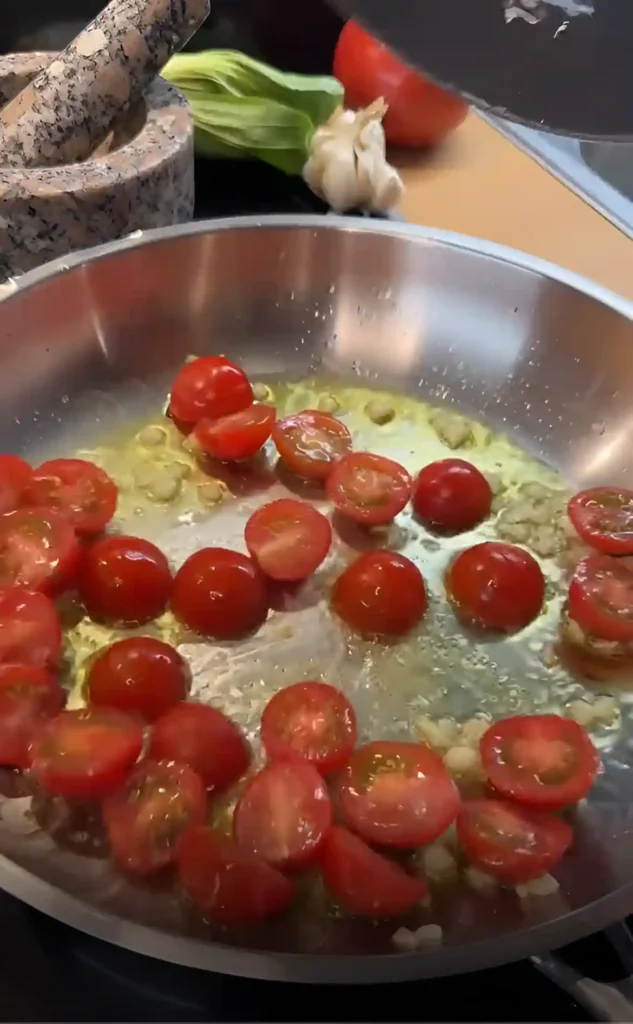 Kirschtomaten brutzeln in Olivenöl mit Knoblauch in der Pfanne – die frische Basis für eine schnelle Tomatensauce zu Ravioli.