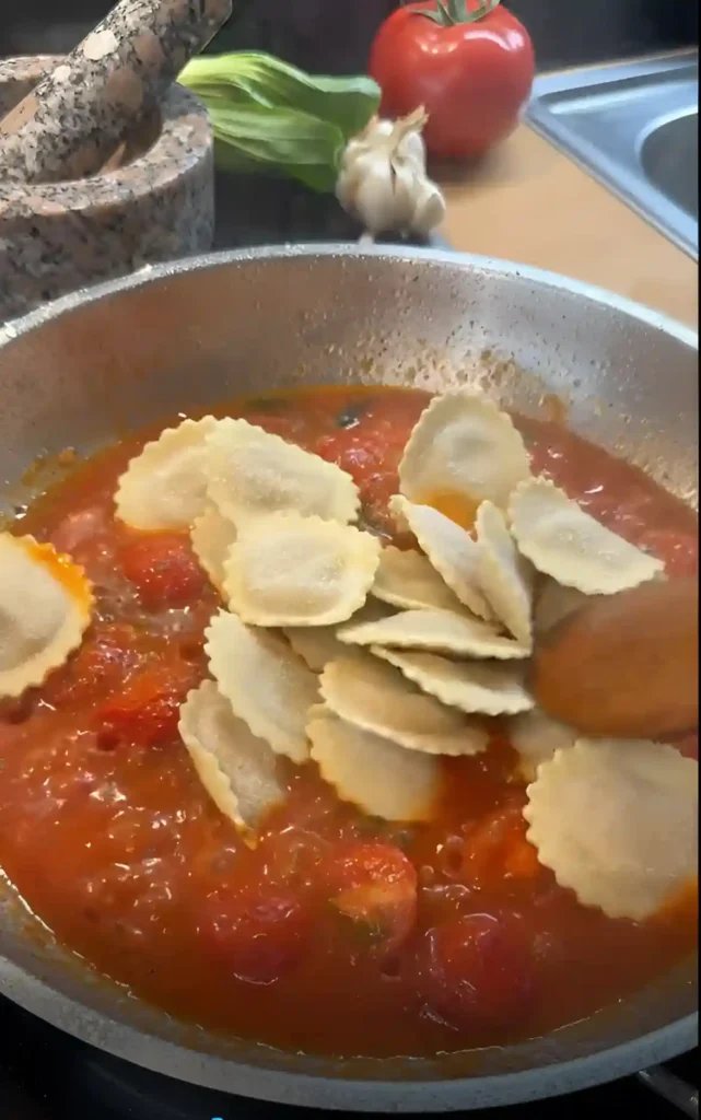 Frische Ravioli werden in eine köchelnde Tomatensauce gegeben – Basis für eine schnelle Sauce zu Ravioli mit Basilikum und Mozzarella.