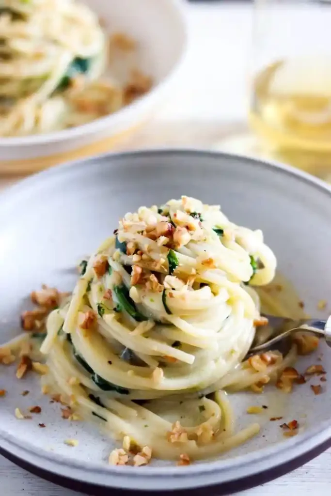 Pasta mit cremiger Avocado-Basilikum-Soße auf weißem Teller, garniert mit Parmesan, Pinienkernen und frischen Kräutern – eine moderne, leckere Soße für Pasta.
