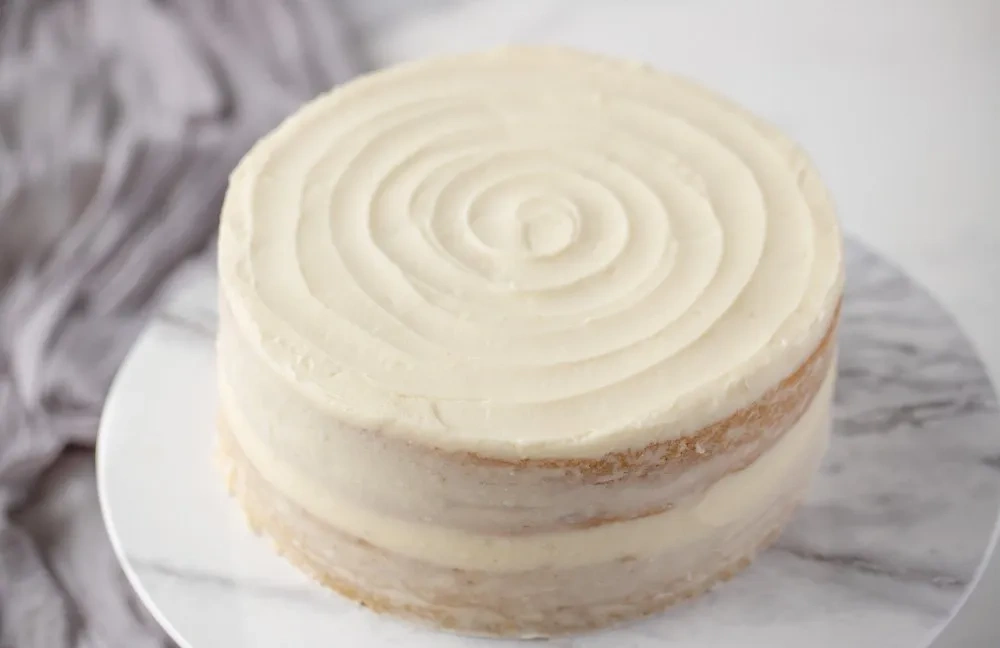 Zweilagige glutenfreie Vanille-Torte mit spiralförmig aufgetragenem Frosting auf Marmorplatte
