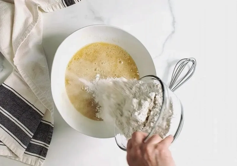 Glutenfreies Mehl wird in eine Schüssel mit aufgeschlagenen Eiern und Zucker für Vanille-Torte eingerührt