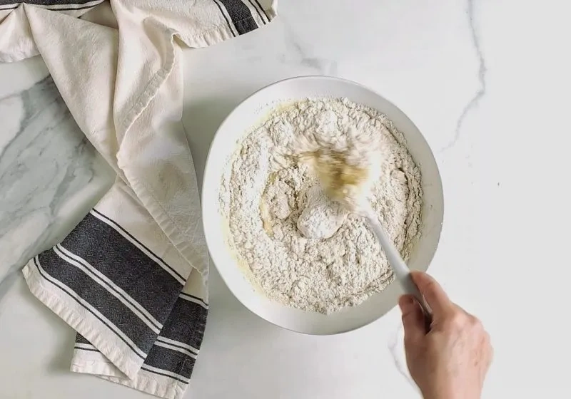 Glutenfreies Mehl wird mit einem Teigschaber in einer Schüssel unter die flüssige Masse gehoben