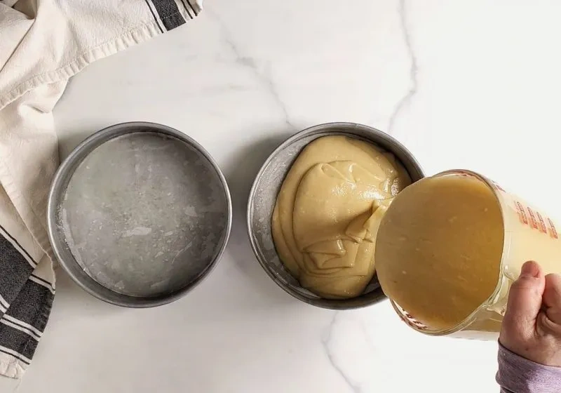 Glutenfreier Kuchenteig wird aus einem Messbecher in eine vorbereitete Springform gegossen
