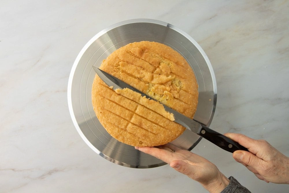 Tortenboden einer glutenfreien Torte wird mit einem langen Messer waagerecht zugeschnitten