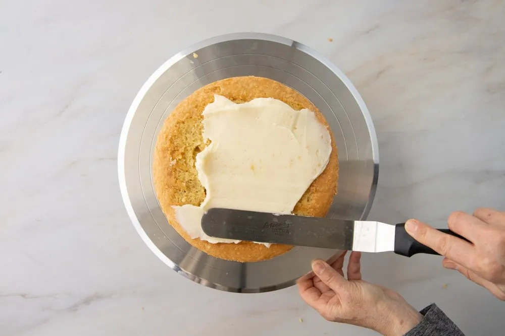 Frosting wird mit einer Winkelpalette auf den unteren Boden einer glutenfreien Torte gestrichen