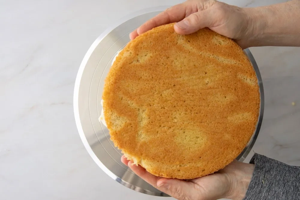 Oberer Boden einer glutenfreien Torte wird vorsichtig auf die mit Frosting bestrichene untere Schicht gesetzt