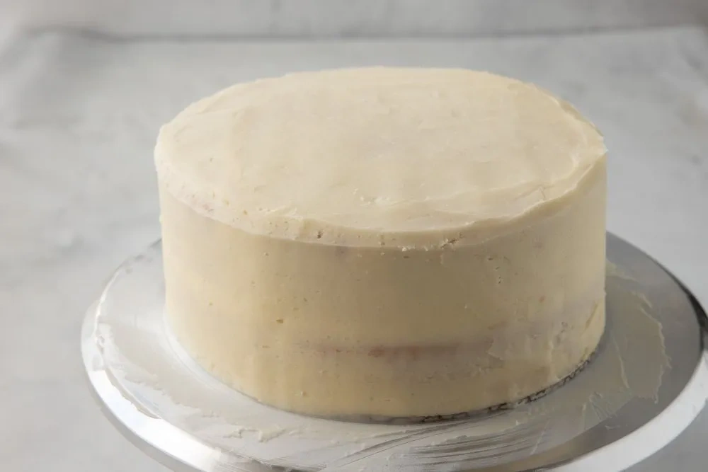 Glatt eingestrichene, zweilagige glutenfreie Torte mit Vanille auf silberner Drehscheibe vor dem Dekorieren