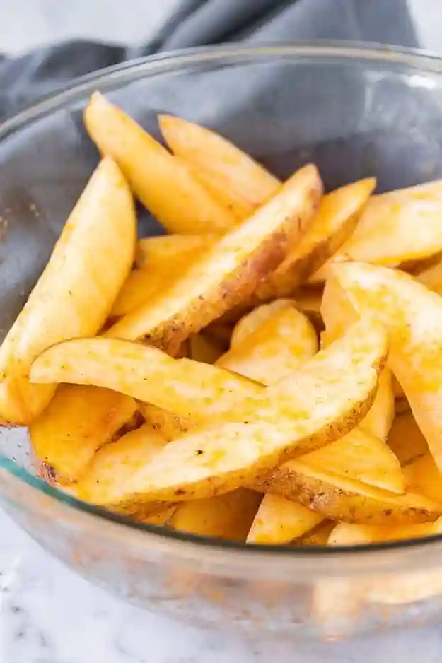 Gewürzte rohe Kartoffelecken in einer Glasschüssel – Vorbereitung für die Heißluftfritteuse