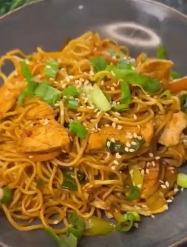 Asiatische gebratene Nudeln mit Gemüse und Hähnchen in Schüssel, mit Sesam und Frühlingszwiebeln garniert