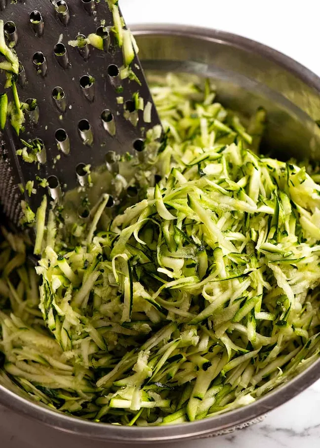 Frisch geriebene Zucchini in einer Metallschüssel – perfekte Vorbereitung für Zucchinisauce für Pasta.

