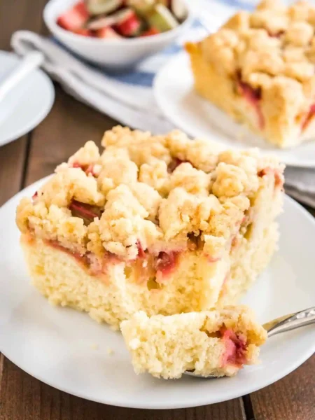 Omas saftiger Rhabarber Streuselkuchen vom Blech mit knusprigen Streuseln und fluffigem Teig, serviert auf einem weißen Teller.