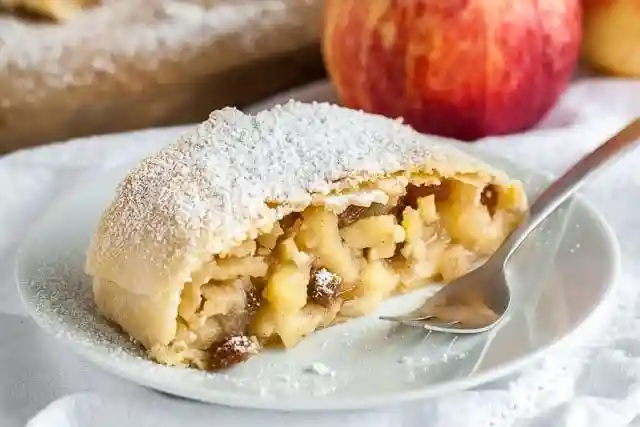 Apfelstrudel Rezept mit Strudelteig – Stück Apfelstrudel mit Rosinen und Puderzucker auf Teller