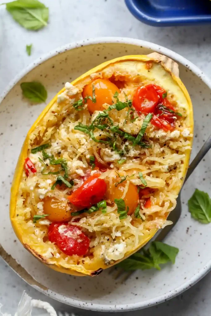 Spaghettikürbis mit Feta und Tomaten im Backofen – servierfertig mit frischem Basilikum.
