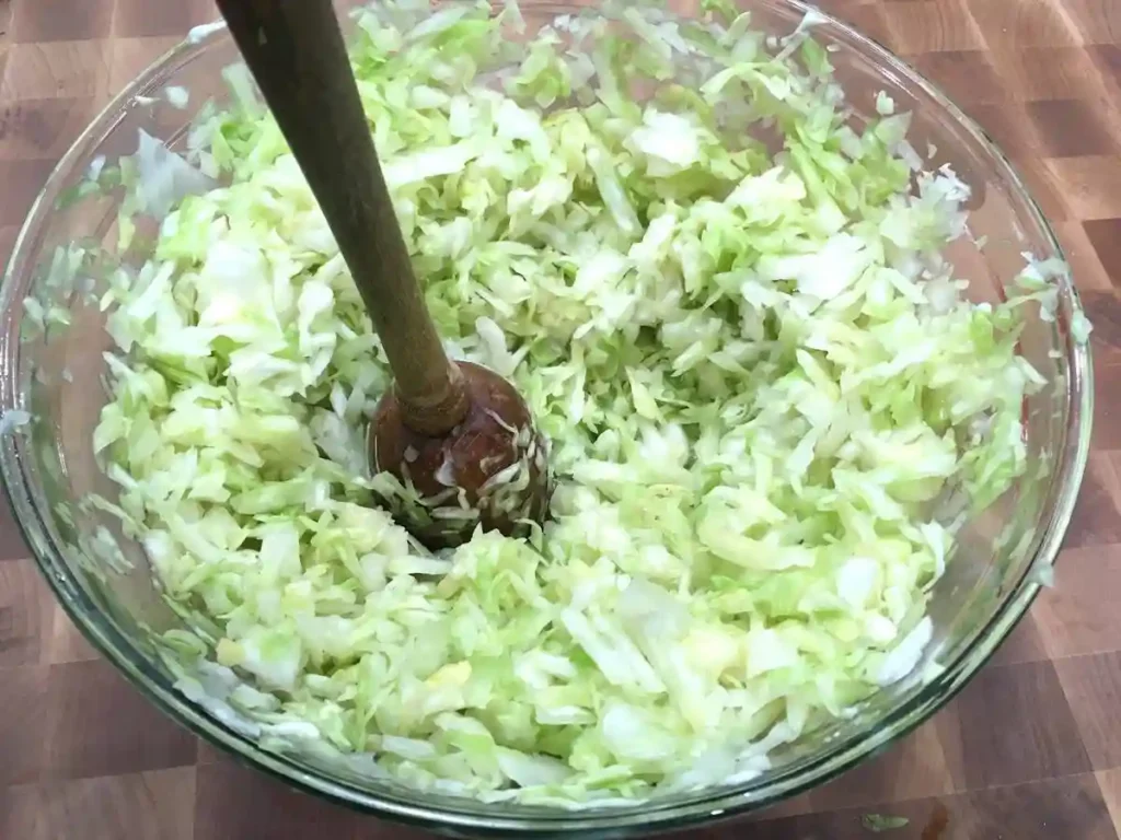 Fein geschnittener Weißkohl mit Holzstampfer – Vorbereitung für Sauerkraut Rezept selber machen