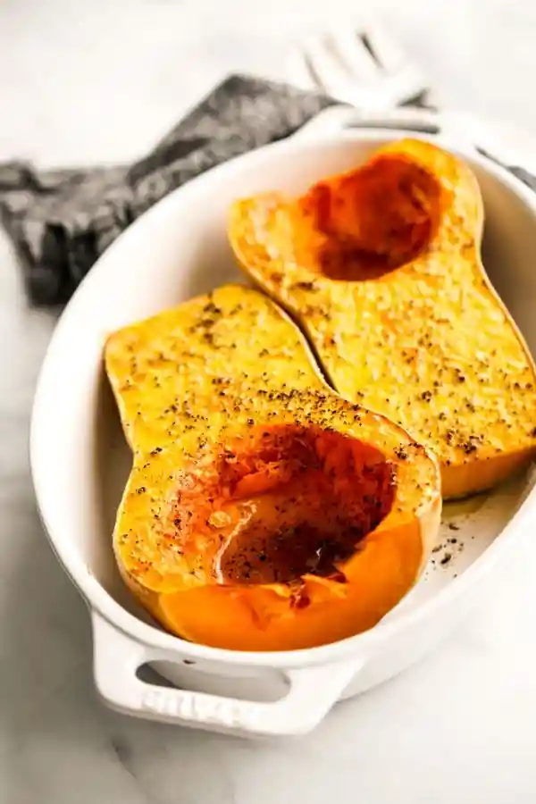 Das Bild zeigt einen halbierten Butternut Kürbis, der in einer Auflaufform liegt und mit Salz, Pfeffer und Gewürzen bestreut wurde. Diese Vorbereitung ist der wichtigste Schritt, bevor der Butternut Kürbis im Ofen mit Schale gebacken wird. So wird das Gemüse aromatisch, innen zart und außen leicht karamellisiert – ein perfektes Butternut Kürbis Ofen Rezept für herbstliche Beilagen oder gesunde Hauptgerichte.