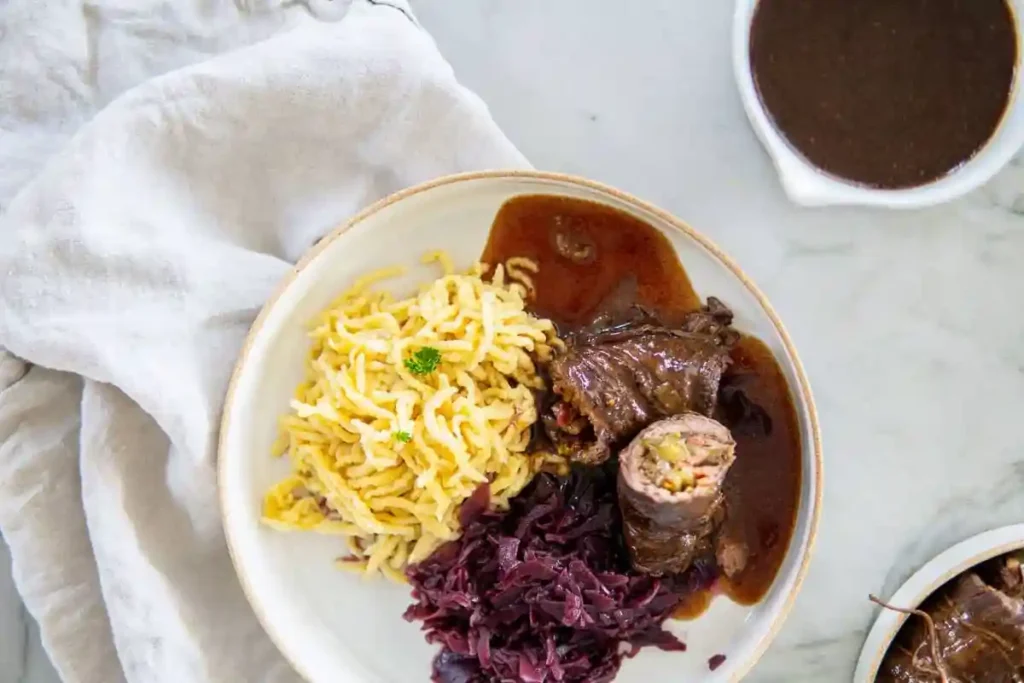Klassische Rinderrouladen mit Soße, Spätzle und Rotkohl auf Teller serviert