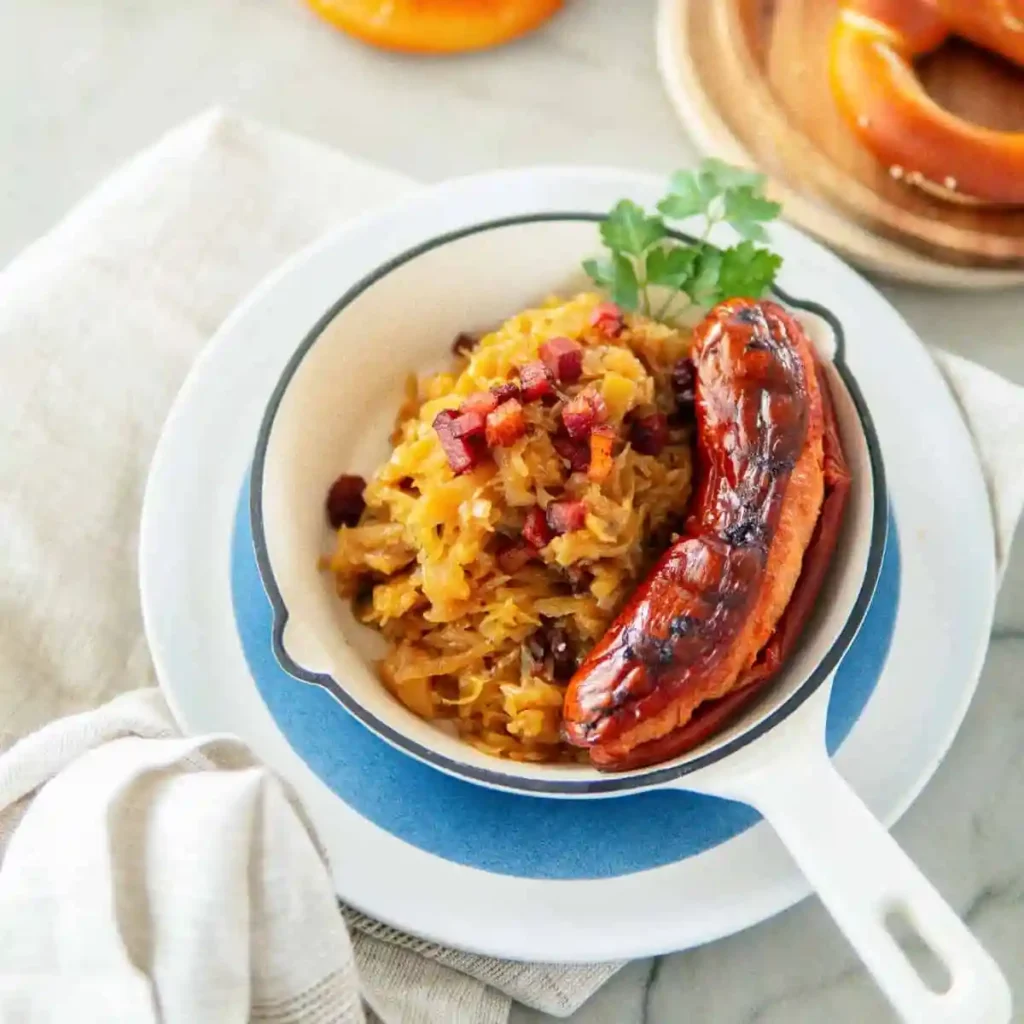 Sauerkraut mit Speck und Zwiebeln serviert mit Bratwurst – deutsches Rezept