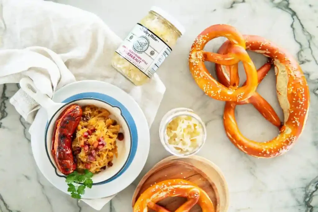 Sauerkraut mit Speck und Zwiebeln serviert mit Bratwurst und Brezeln – deutsches Rezept