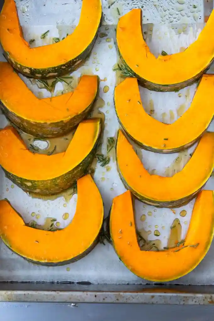Rohe Kürbisspalten mit Öl und Rosmarin auf Backblech – Kürbis im Ofen Rezept