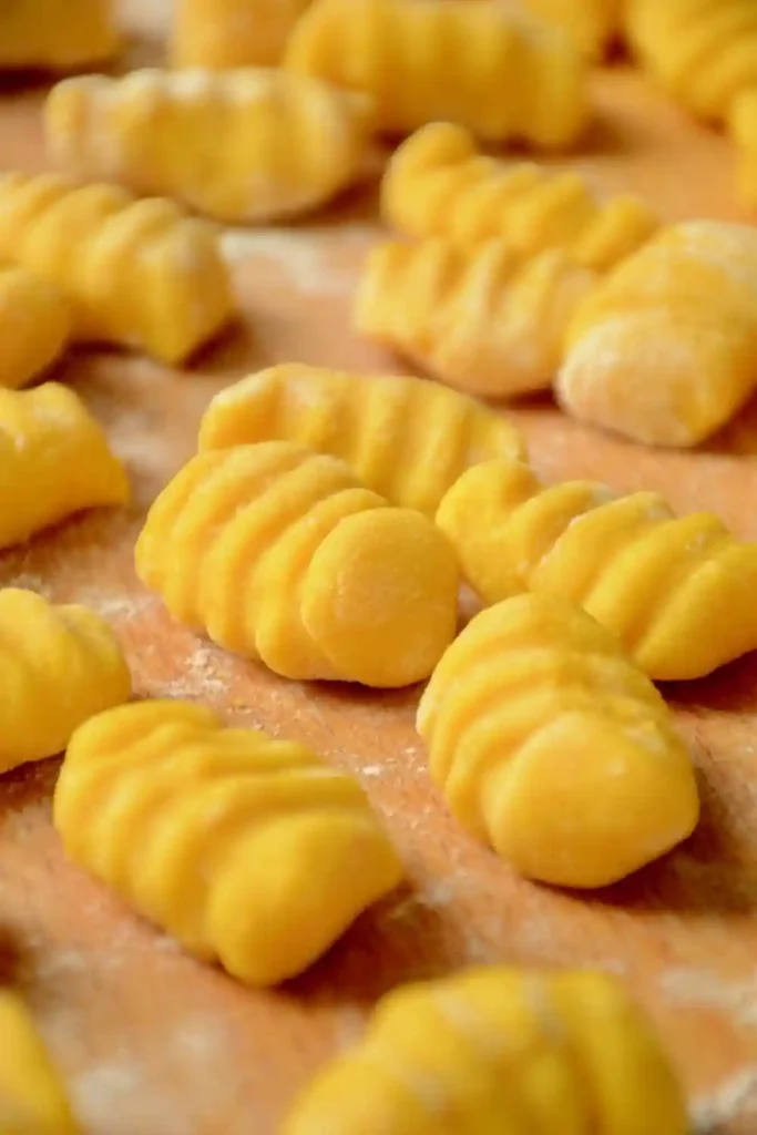 Frisch geformte Kürbis Gnocchi mit typischer Rillenform auf bemehltem Holzbrett