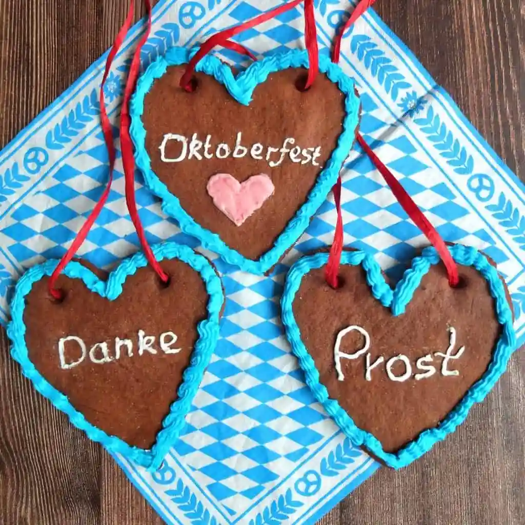 Lebkuchenherz mit blauer Zuckerguss-Dekoration und rotem Band – selbstgemachte Lebkuchenherzen mit Aufschriften „Oktoberfest“, „Prost“ und „Danke“.