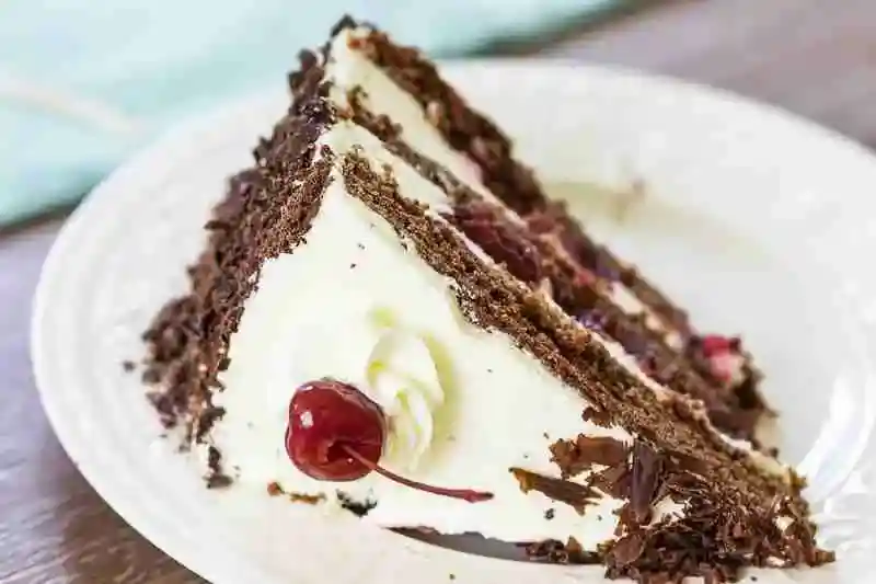 Original Schwarzwälder Kirschtorte Rezept mit Schlagsahne – angeschnittenes Tortenstück mit Kirschen und Schokoladenraspeln