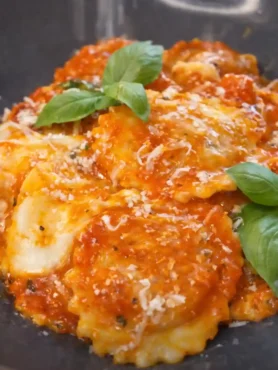 Ravioli mit Tomatensauce auf dunklem Teller, serviert mit Basilikum und Parmesan – klassische Soßen zu Ravioli
