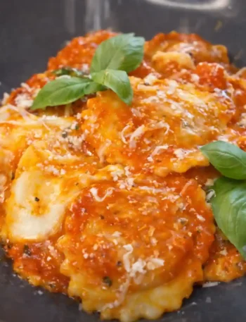 Ravioli mit Tomatensauce auf dunklem Teller, serviert mit Basilikum und Parmesan – klassische Soßen zu Ravioli