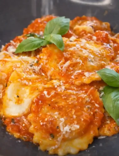 Ravioli mit Tomatensauce auf dunklem Teller, serviert mit Basilikum und Parmesan – klassische Soßen zu Ravioli