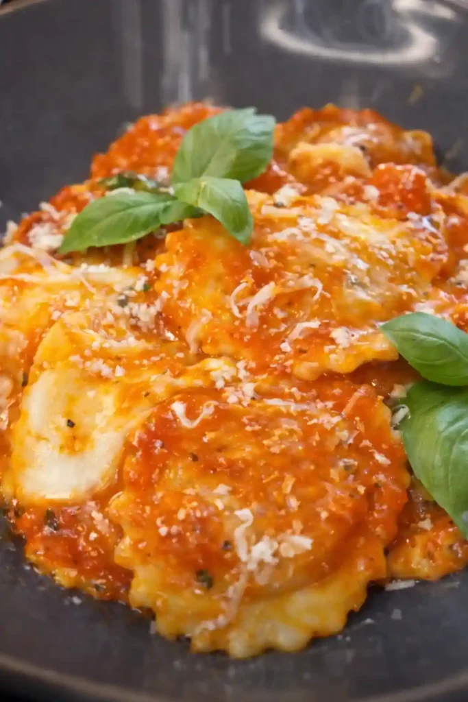 Ravioli mit Tomatensauce auf dunklem Teller, serviert mit Basilikum und Parmesan – klassische Soßen zu Ravioli