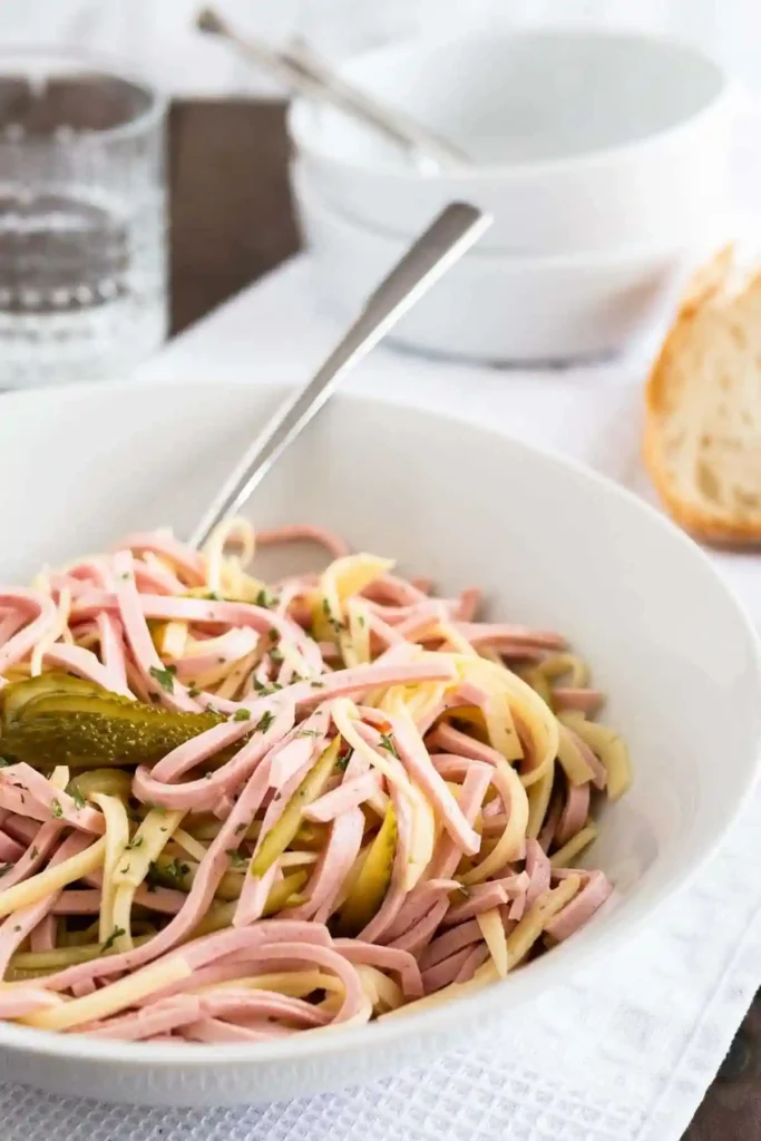 Original bayrischer Wurstsalat Rezept mit Käse und Dressing in einer Schüssel mit Brot serviert