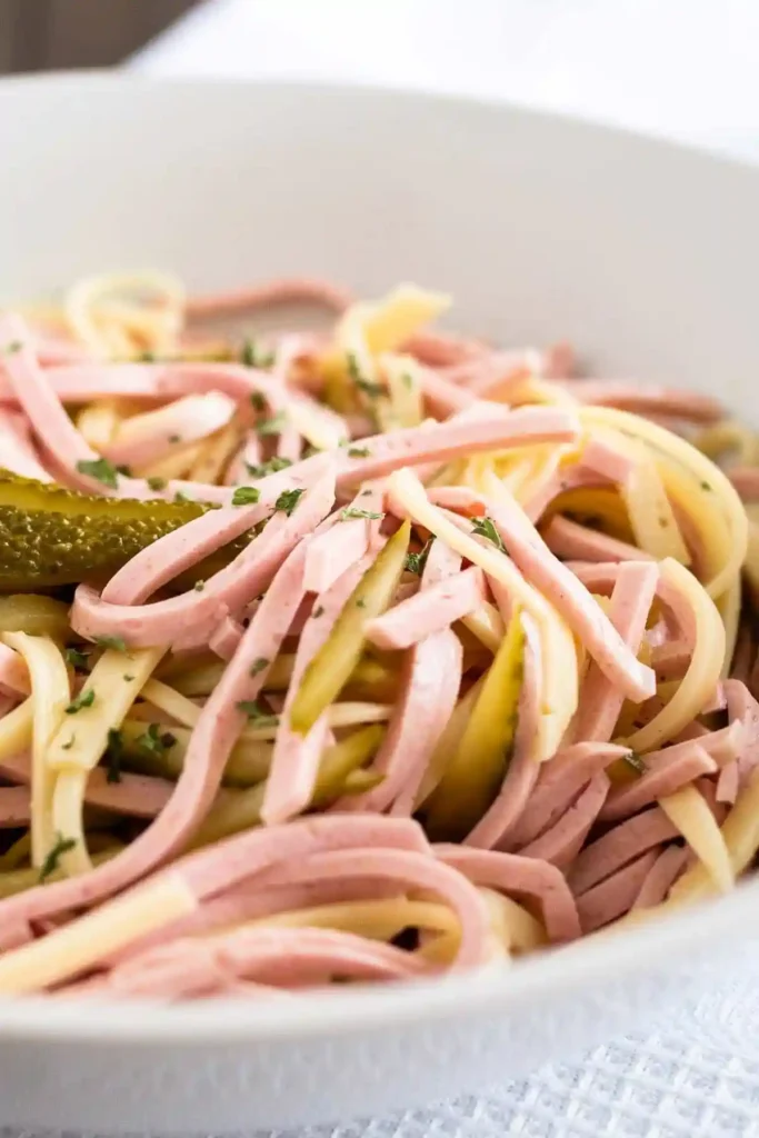 Original bayrischer Wurstsalat Rezept mit Käse und Dressing in einer Schüssel serviert