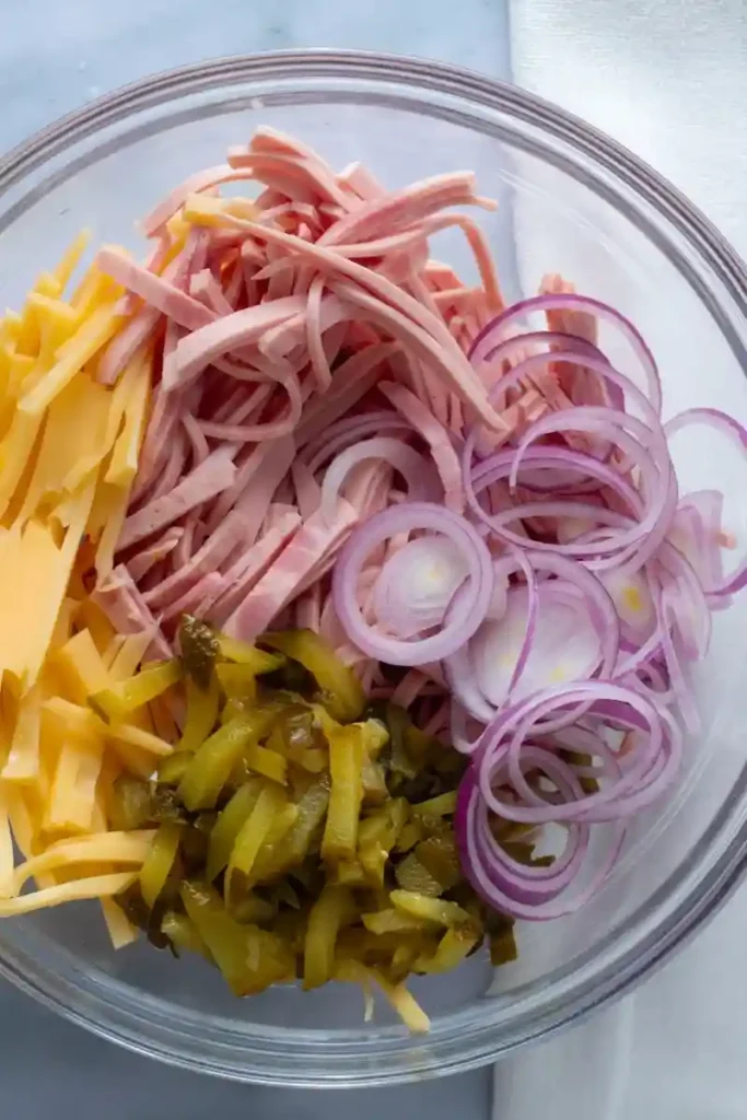 Zutaten für original bayrischer Wurstsalat Rezept mit Käse und Dressing in einer Schüssel vorbereitet