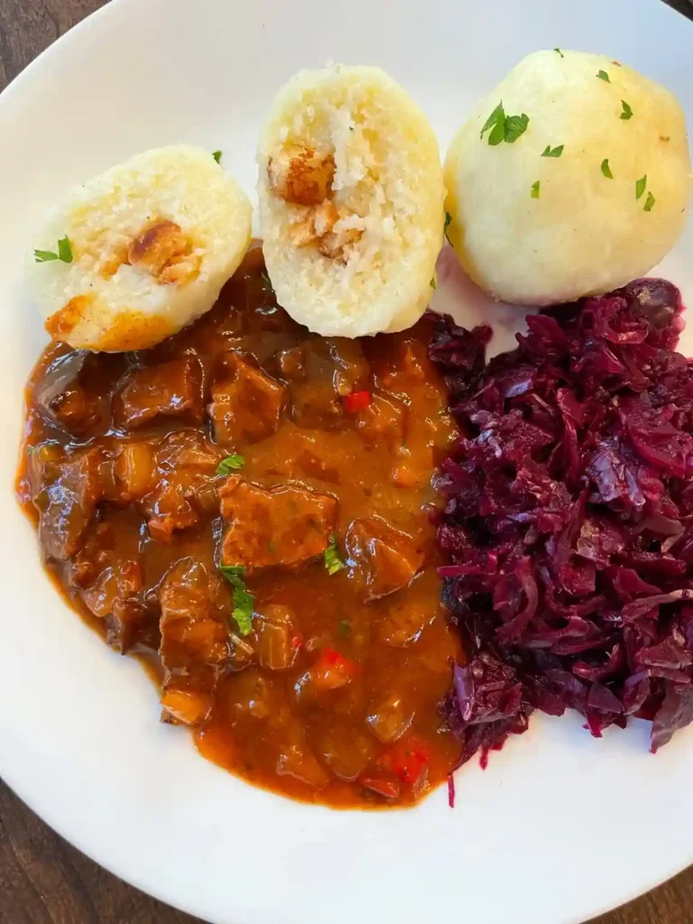 Gulasch Rezept original mit Rindfleisch serviert mit Kartoffelklößen und Rotkohl – klassische Beilage zu Rindergulasch