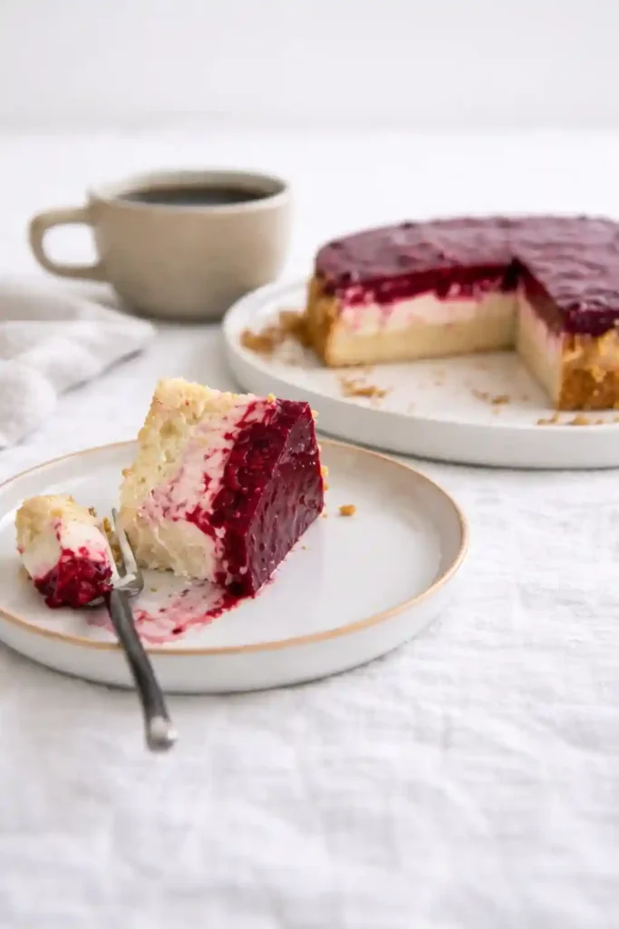 Stück Himbeertorte mit Sahne auf Teller – einfache Himbeer-Sahne-Torte mit Biskuitboden, Cremefüllung und fruchtigem Himbeerbelag neben einer Tasse Kaffee