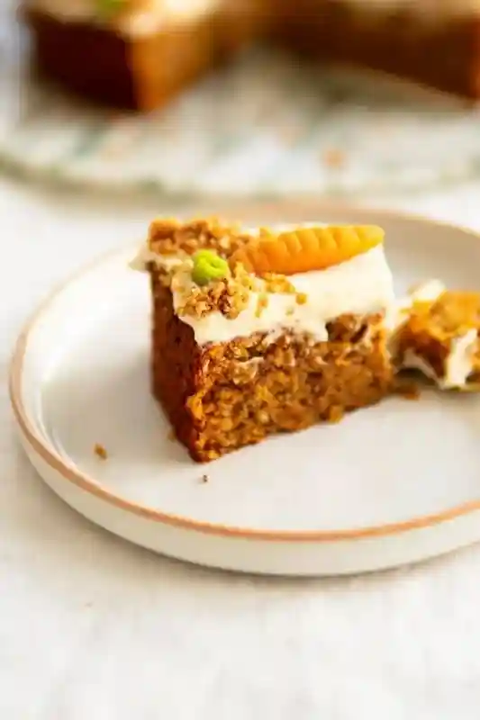Saftiges Stück Karottenkuchen mit Frischkäse-Frosting, Rüblikuchen mit Nüssen und Marzipanmöhre auf Teller
