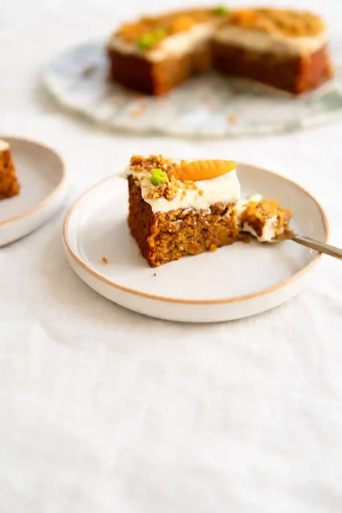 Stück saftiger Karottenkuchen mit Frischkäse-Frosting, klassischer Rüblikuchen mit Nüssen und Marzipanmöhre