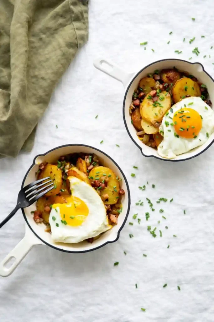 Knusprige Bratkartoffeln mit Speck und Zwiebeln in Pfanne mit Spiegelei