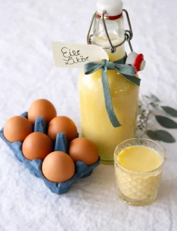 Omas Eierlikör Rezept DDR – selbstgemachter Eierlikör mit Rum in Glasflasche, daneben frische Eier und ein Likörglas