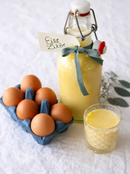 Omas Eierlikör Rezept DDR – selbstgemachter Eierlikör mit Rum in Glasflasche, daneben frische Eier und ein Likörglas