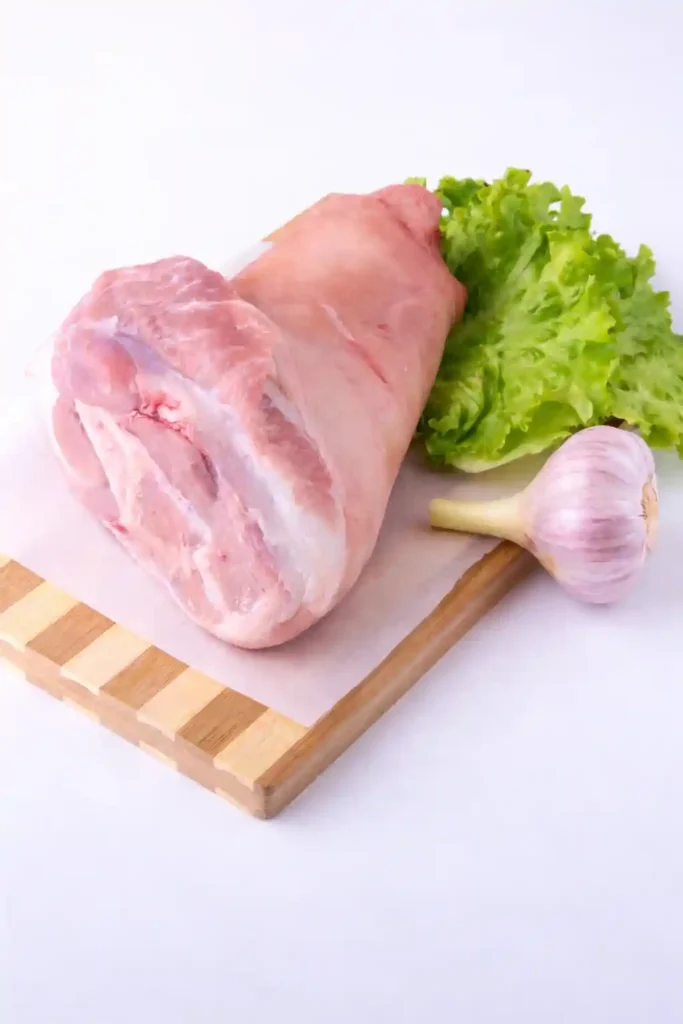 Rohe Schweinshaxe für Schweinshaxe im Backofen mit Vorkochen, frische Haxe auf Schneidebrett mit Knoblauch und Salat