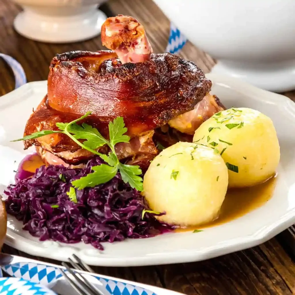 Knusprige bayerische Schweinshaxe im Backofen mit Vorkochen, serviert mit Rotkohl, Kartoffelklößen und Bratensoße