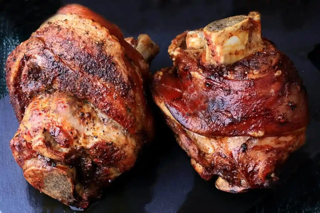 Dieses Bild zeigt die Schweinshaxe Zubereitung Schritt für Schritt: links wird die vorgekochte Haxe gewürzt und vorbereitet, rechts brät die Schweinshaxe im Backofen knusprig aus. Durch das Vorkochen und das anschließende Rösten im Ofen entsteht eine knusprige Schweinshaxe im Backofen mit saftigem Fleisch und krosser Kruste – typisch für ein traditionelles bayerisches Schweinshaxe Rezept.