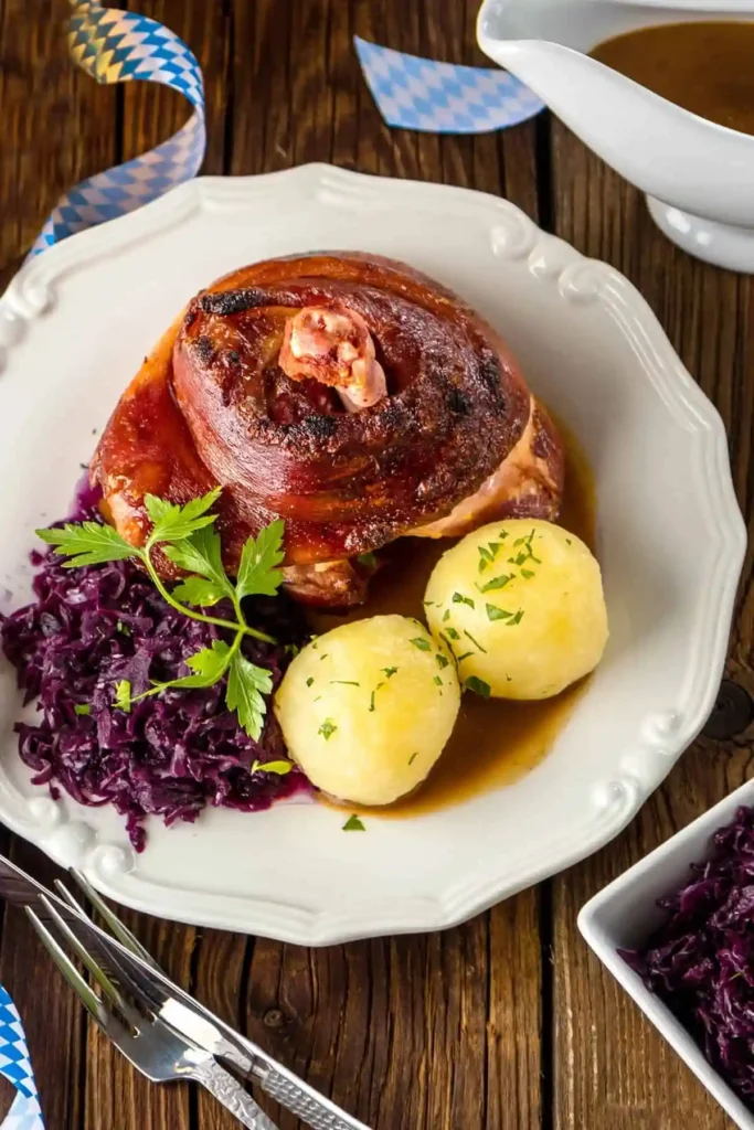Diese bayerische Schweinshaxe im Backofen mit Vorkochen zeigt eine perfekt gebratene, knusprige Haxe im Ofen mit saftigem Fleisch und aromatischer Soße. Das traditionelle Schweinshaxe Rezept wird mit Rotkohl und Kartoffelklößen serviert und steht für echte bayerische Küche.
