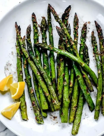 Grüner Spargel grillen mit Marinade – gegrillter Spargel vom Grill mit Zitronenspalten auf einem Teller