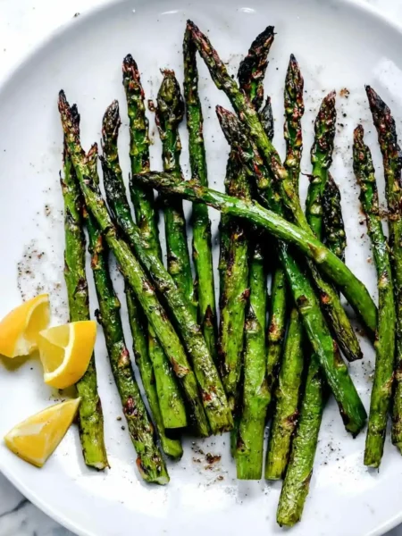 Grüner Spargel grillen mit Marinade – gegrillter Spargel vom Grill mit Zitronenspalten auf einem Teller