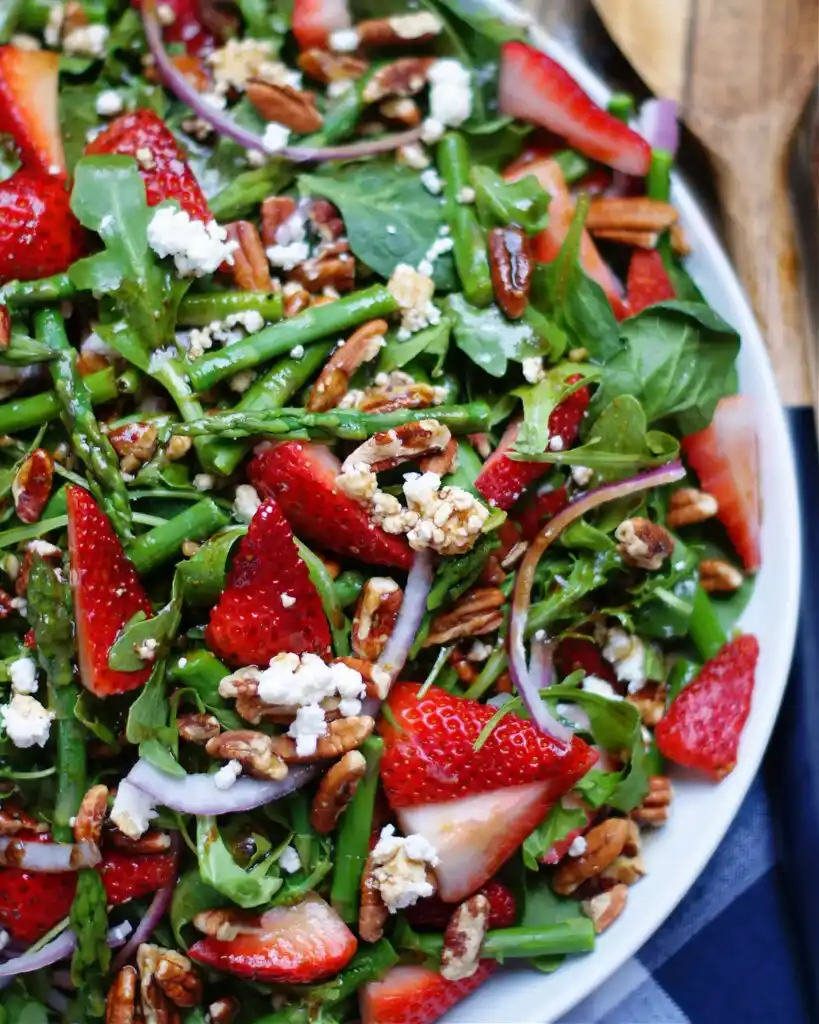 Frischer grüner spargelsalat mit erdbeeren und balsamico mit feta, rucola und pekannüssen serviert