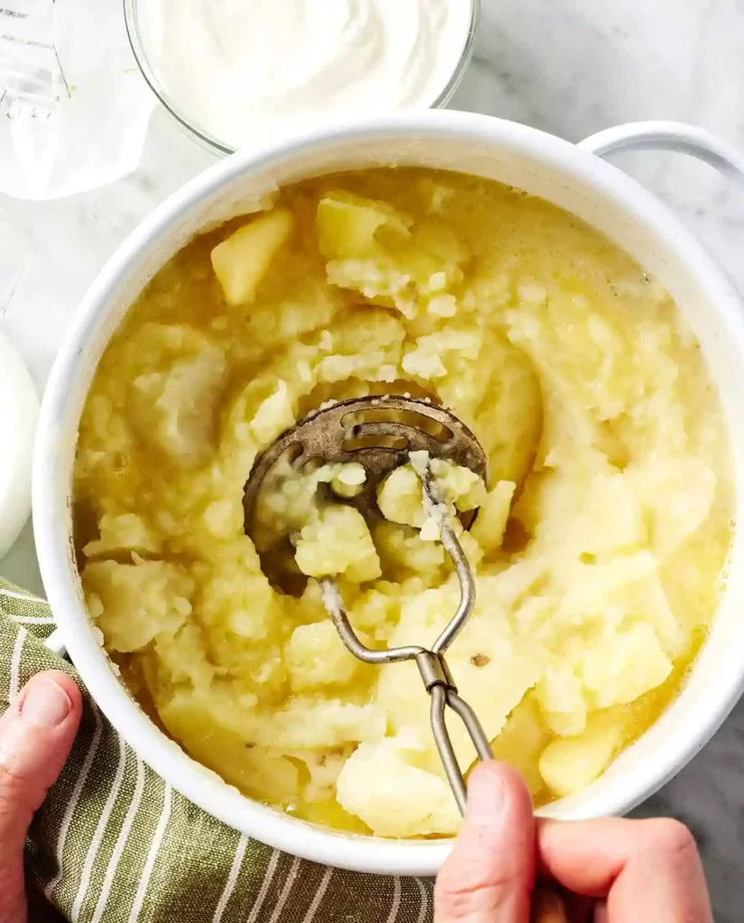 Gekochte Kartoffeln werden mit einem Kartoffelstampfer zerdrückt – Schritt im Kartoffelpüree Rezept zum Kartoffelpüree selber machen